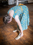 Person in a blue dress with yellow patterns on a wooden floor